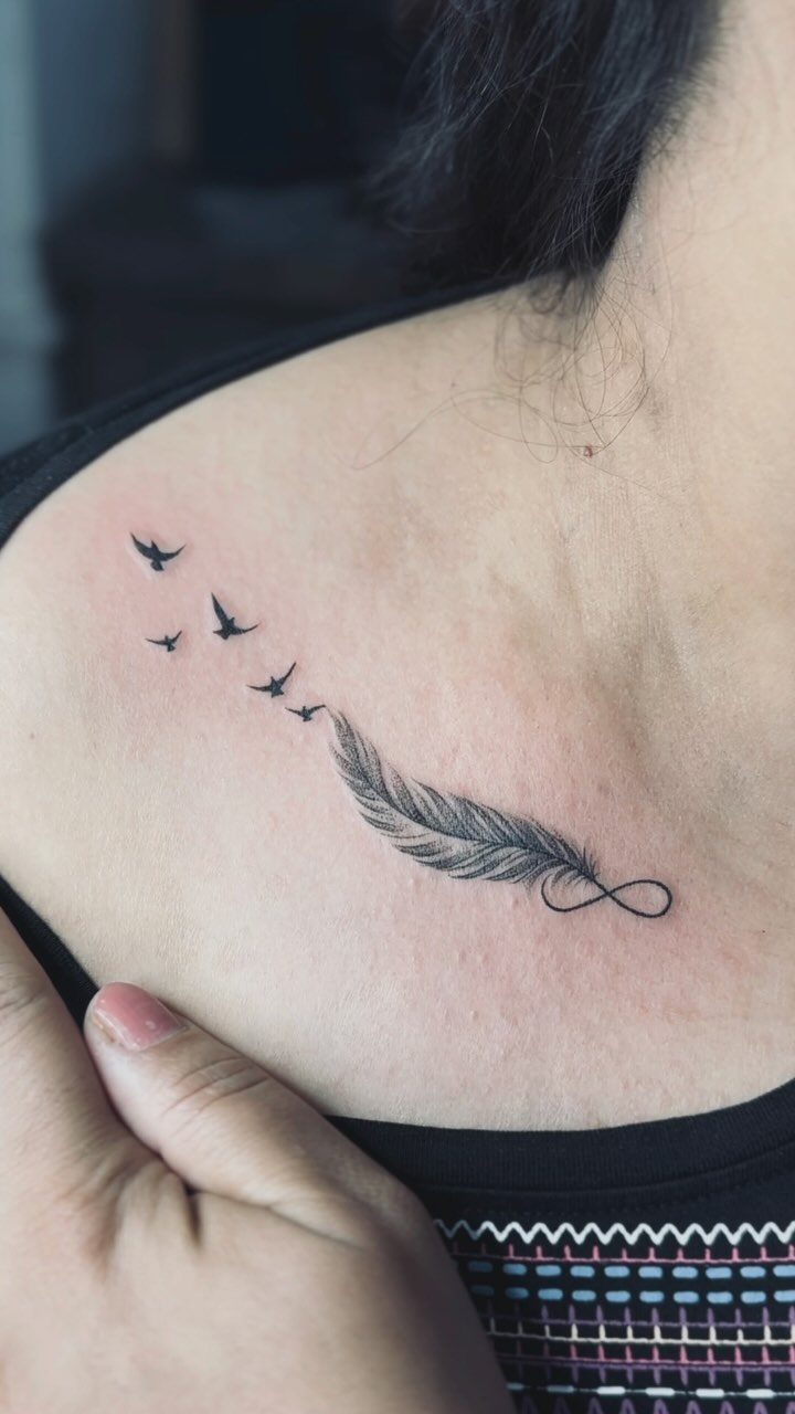 Feather tattoo on a shoulder transitioning into an infinity symbol with flying birds.