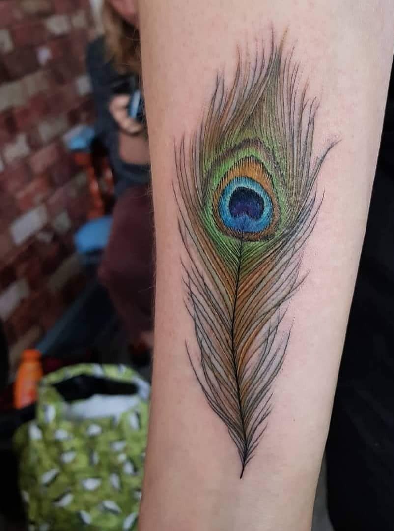 Peacock feather tattoo with blue and green eye on a person's forearm