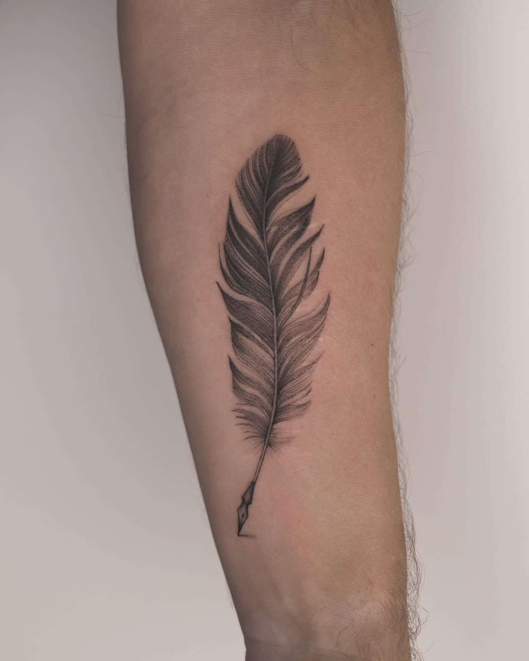 Quill feather tattoo with a writing nib on a person's forearm