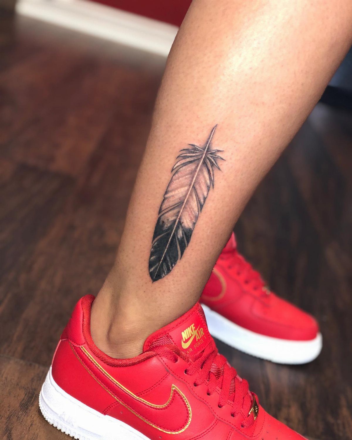 Single feather tattoo on a lower leg above red Nike sneakers