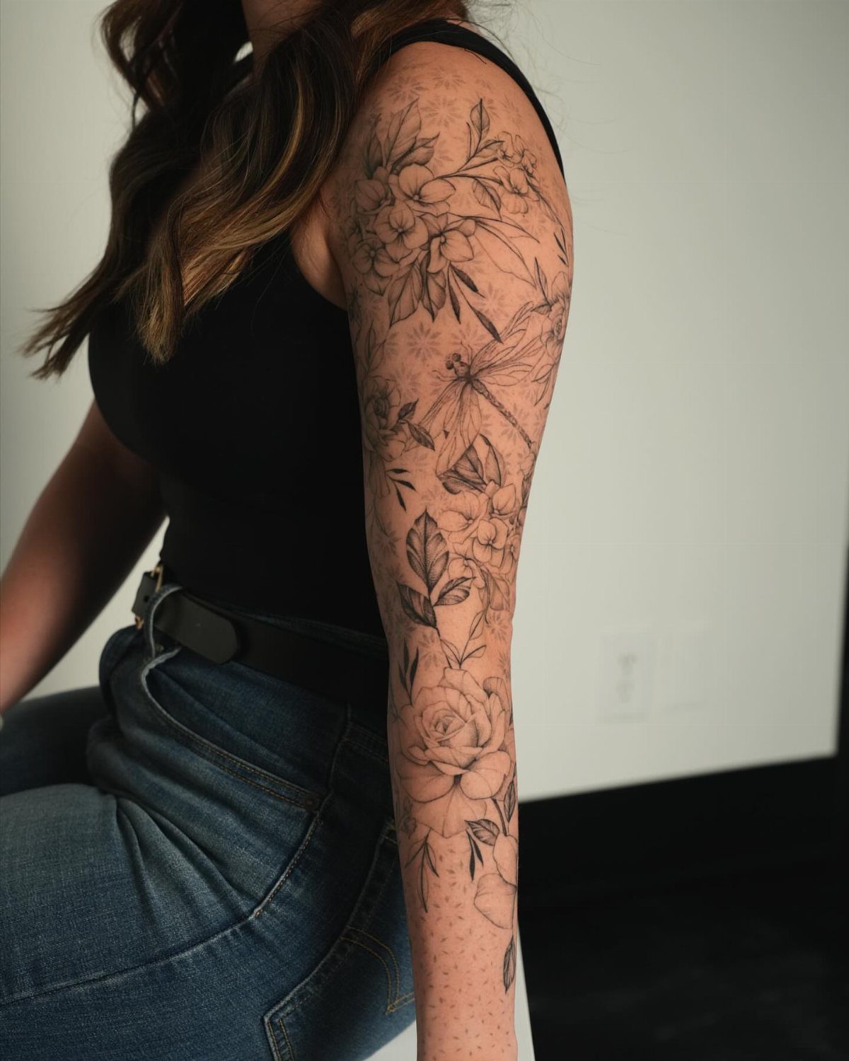 Fine line floral sleeve tattoo covering a person's arm from shoulder to forearm.