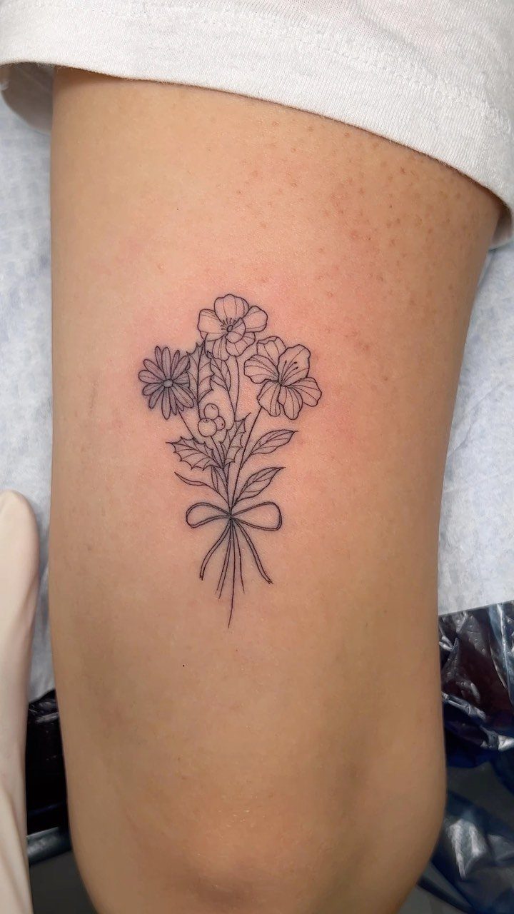 Fine line flower bouquet tattoo tied with a bow on a person's thigh