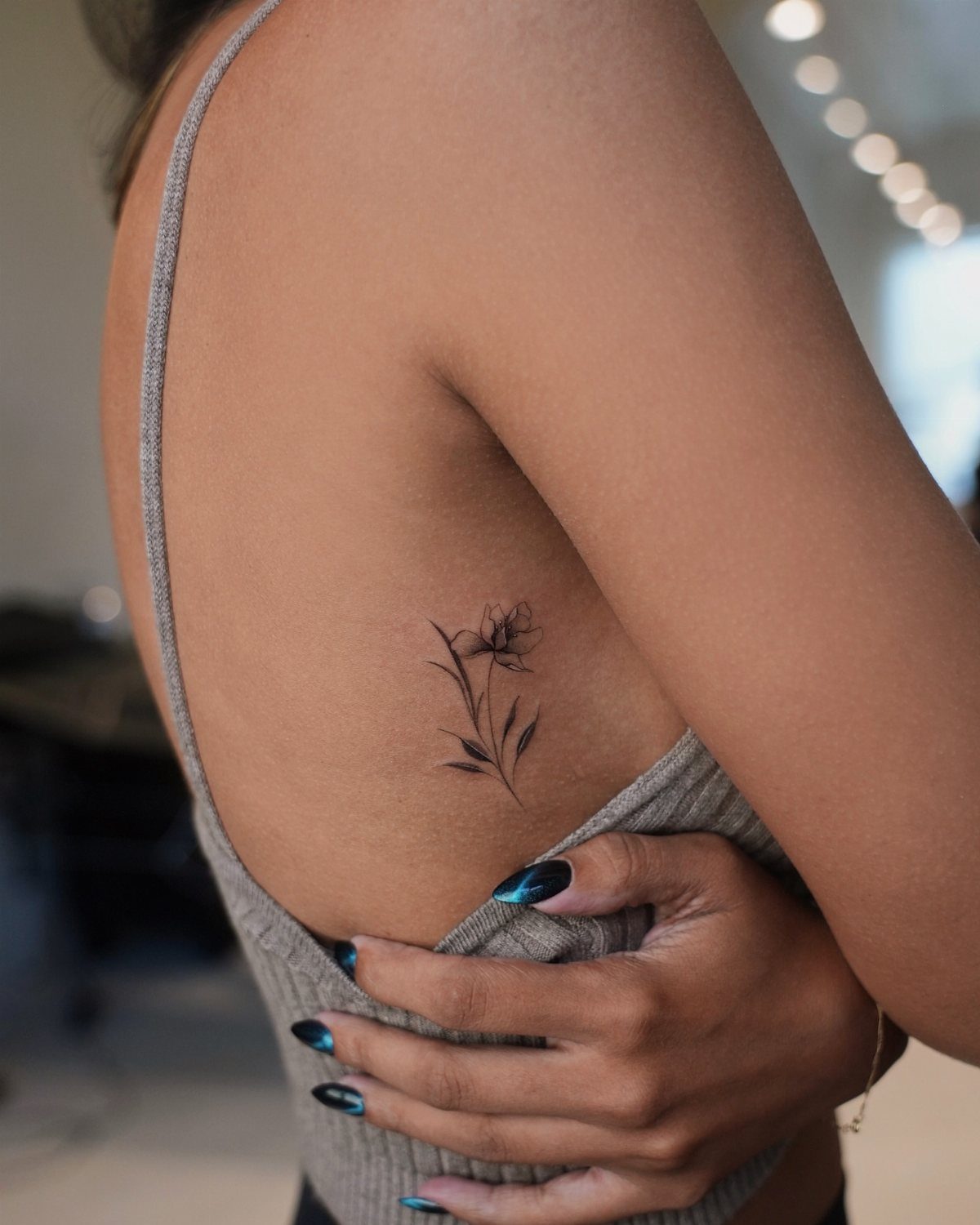 Fine line flower tattoo on a person's ribs with a grey tank top.
