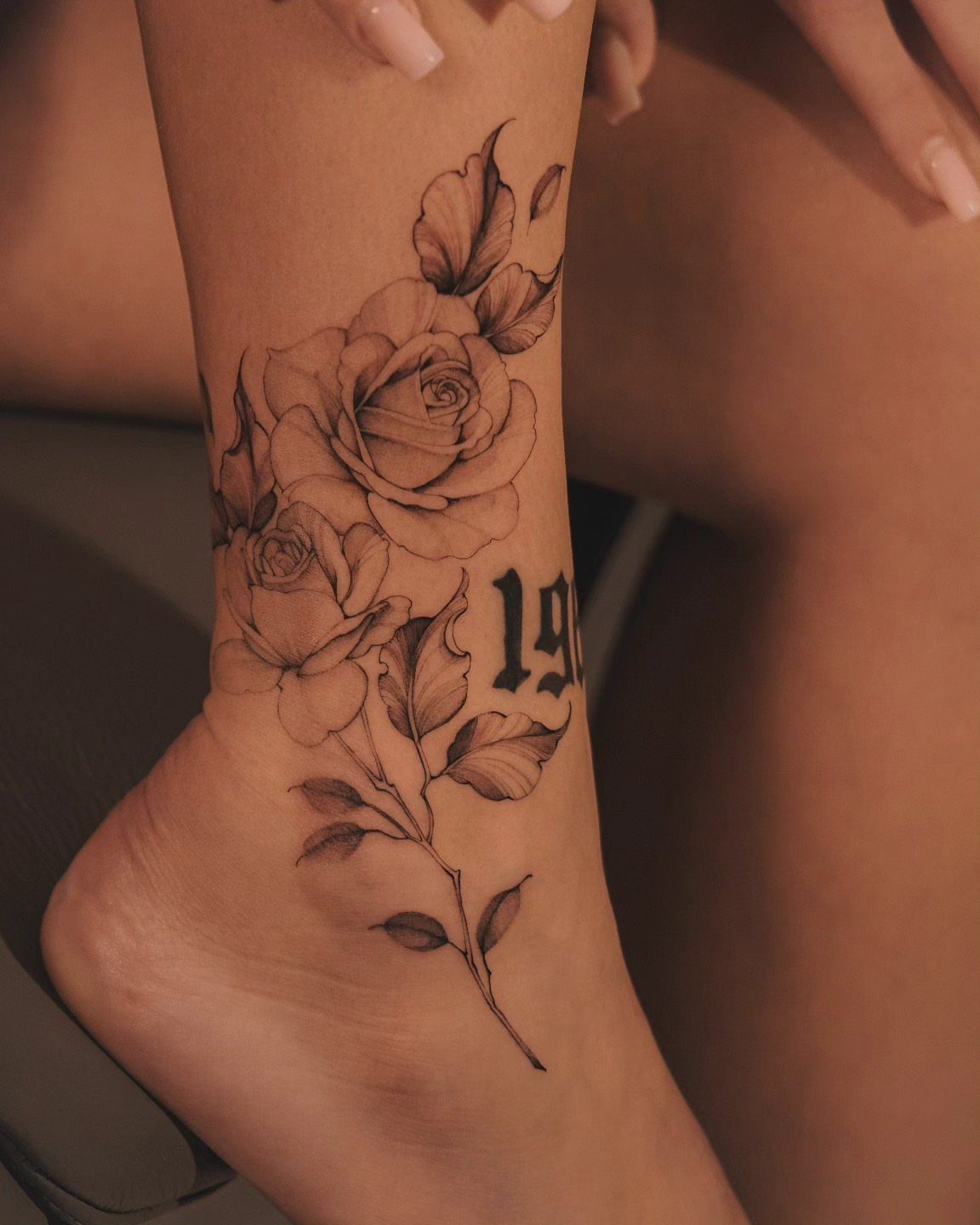 Rose tattoo with leaves and gothic numbers on a person's ankle