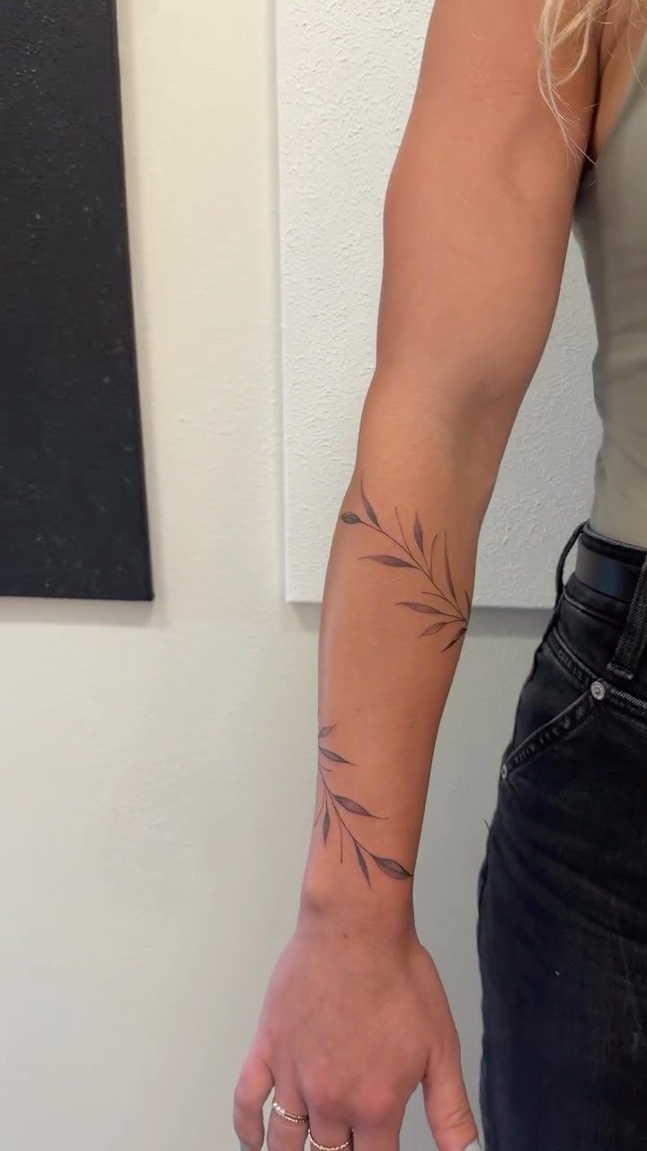Botanical leafy branch tattoos on a person's forearm and wrist in fine line style.