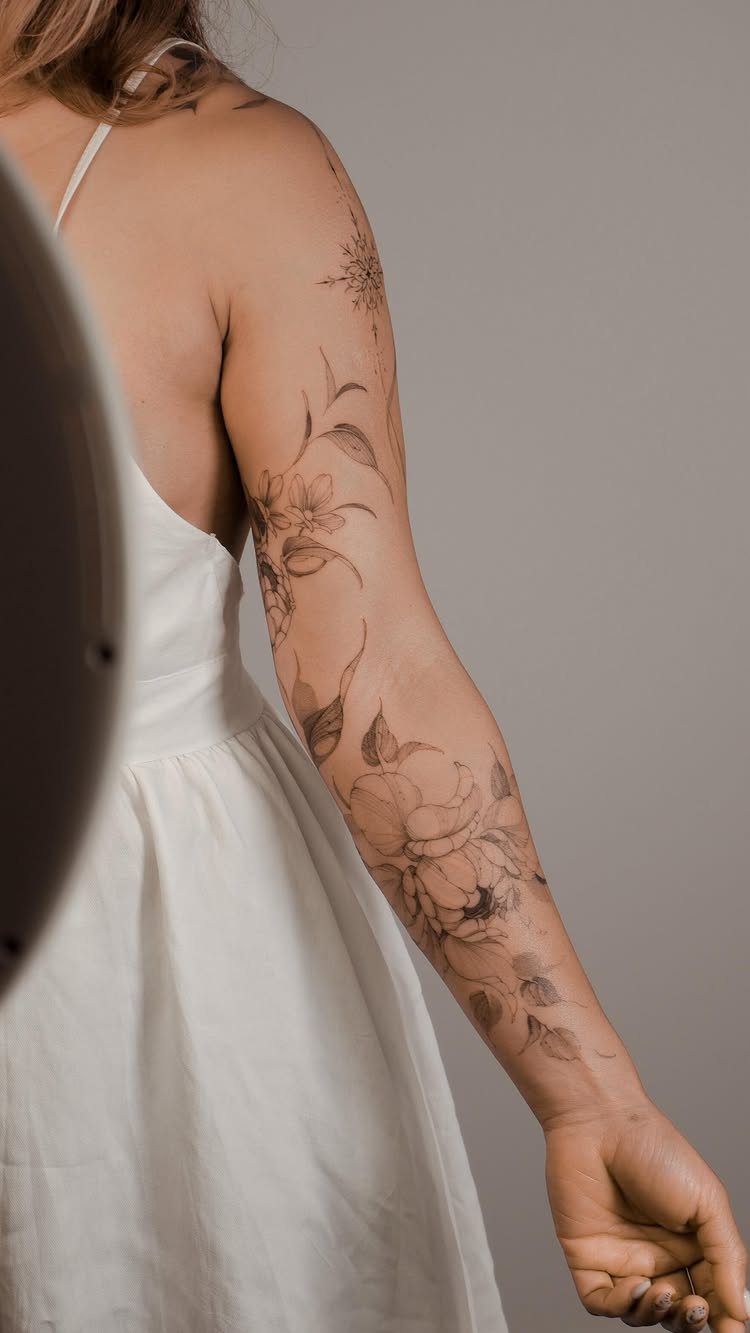 Vertical flower arrangement tattoo on a person's arm with delicate fine line details.