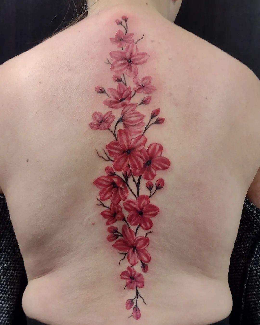 Red blossom tattoo trailing vertically down the spine of a person's back.