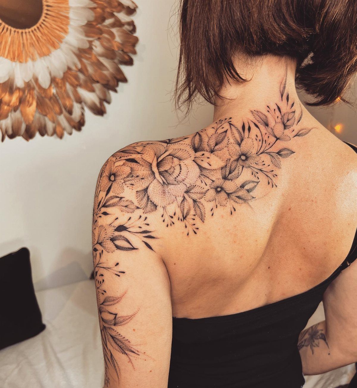 Floral dotwork tattoo on a woman's shoulder and upper back with stippled shading.