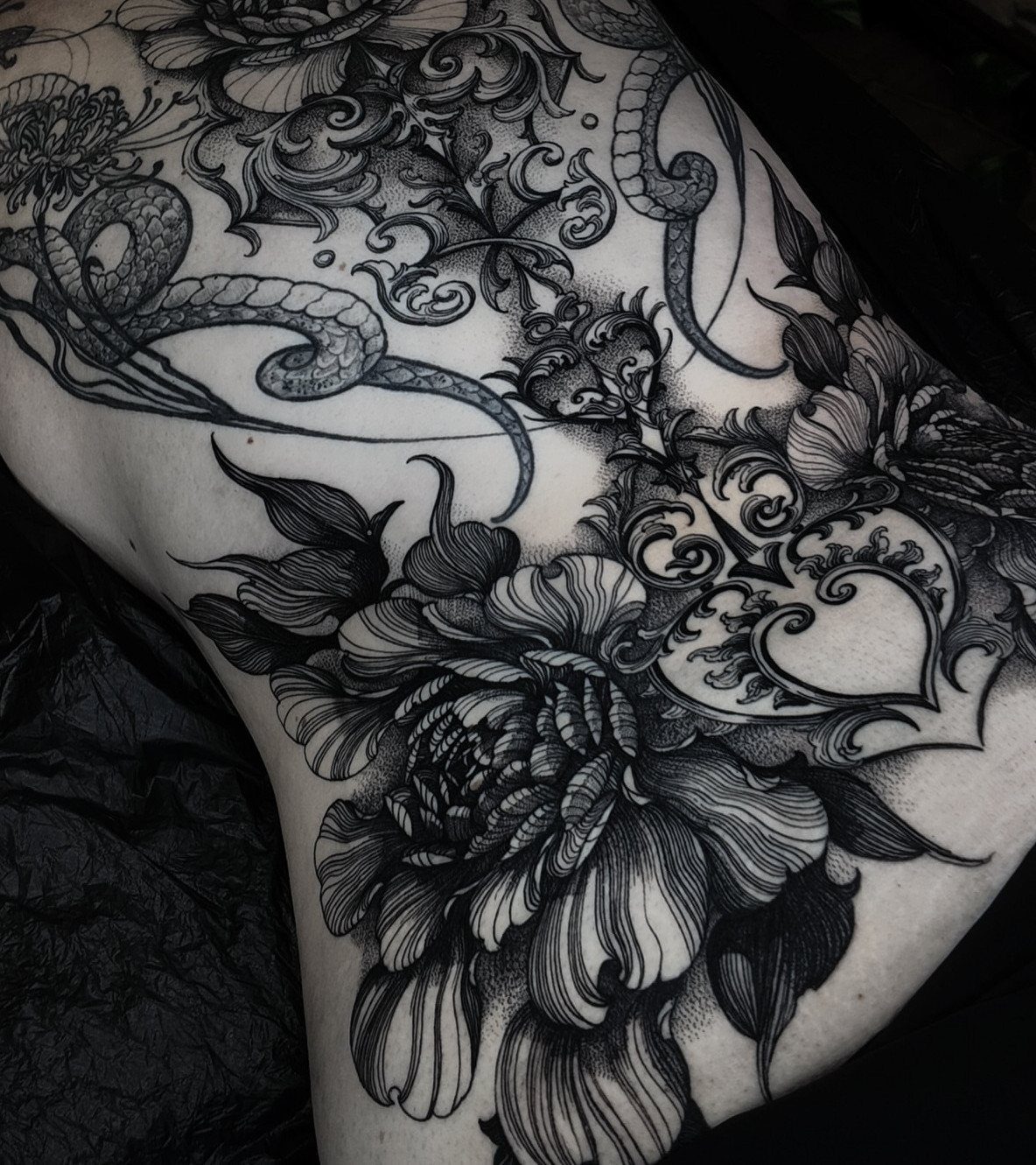 Detailed black and grey peony and serpent tattoo covering a person's back
