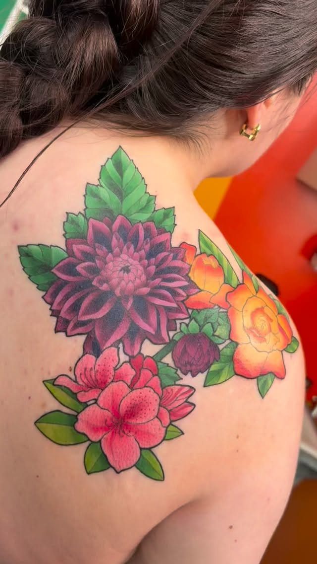 Colorful floral tattoo featuring purple, pink, and yellow flowers on a shoulder blade.