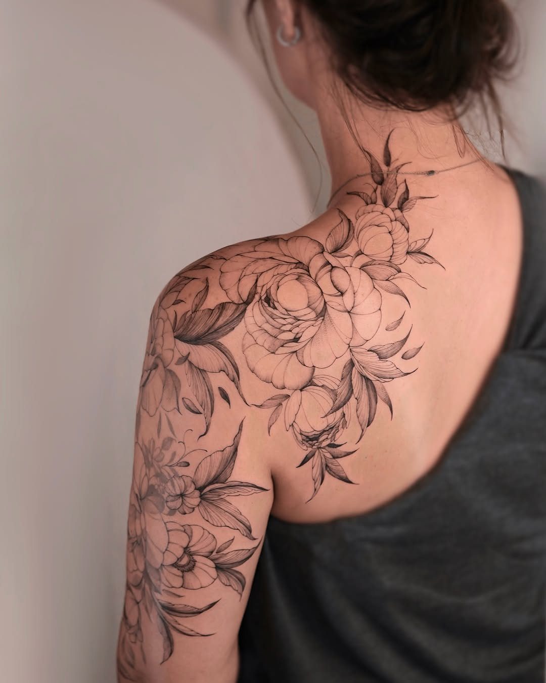 Large floral tattoo of peonies draping across a woman's shoulder and upper back.