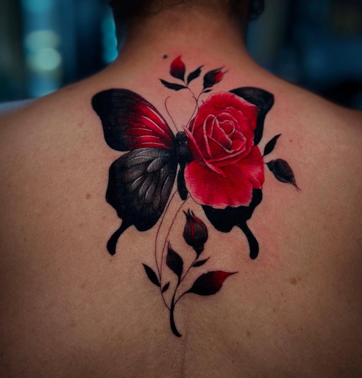 Red rose and black butterfly wing tattoo centered on a person's upper back