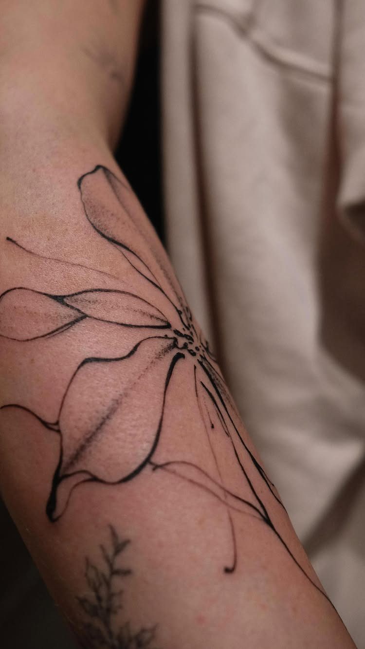 Abstract black ink flower tattoo with flowing lines on a person's forearm