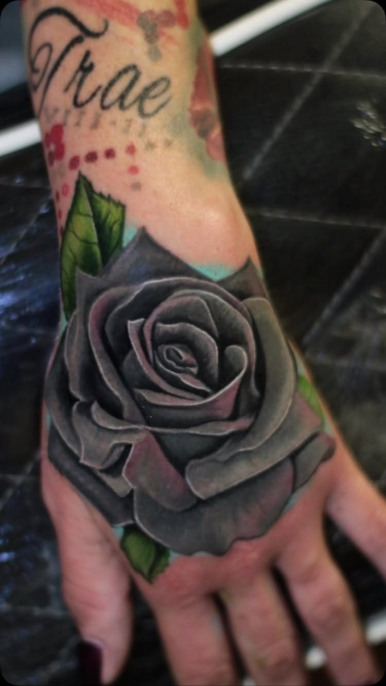 Black rose tattoo with green leaves on the back of a hand