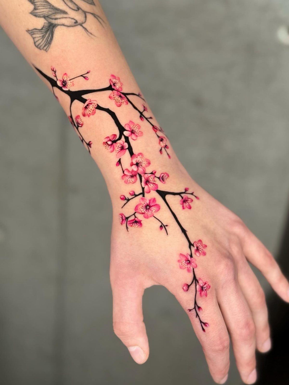 Cherry blossom branch tattoo with pink flowers on a person's wrist and hand.