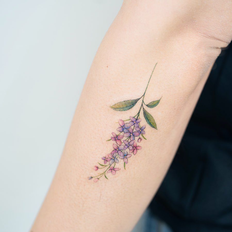 Lilac flower tattoo with purple blossoms and green leaves on a forearm