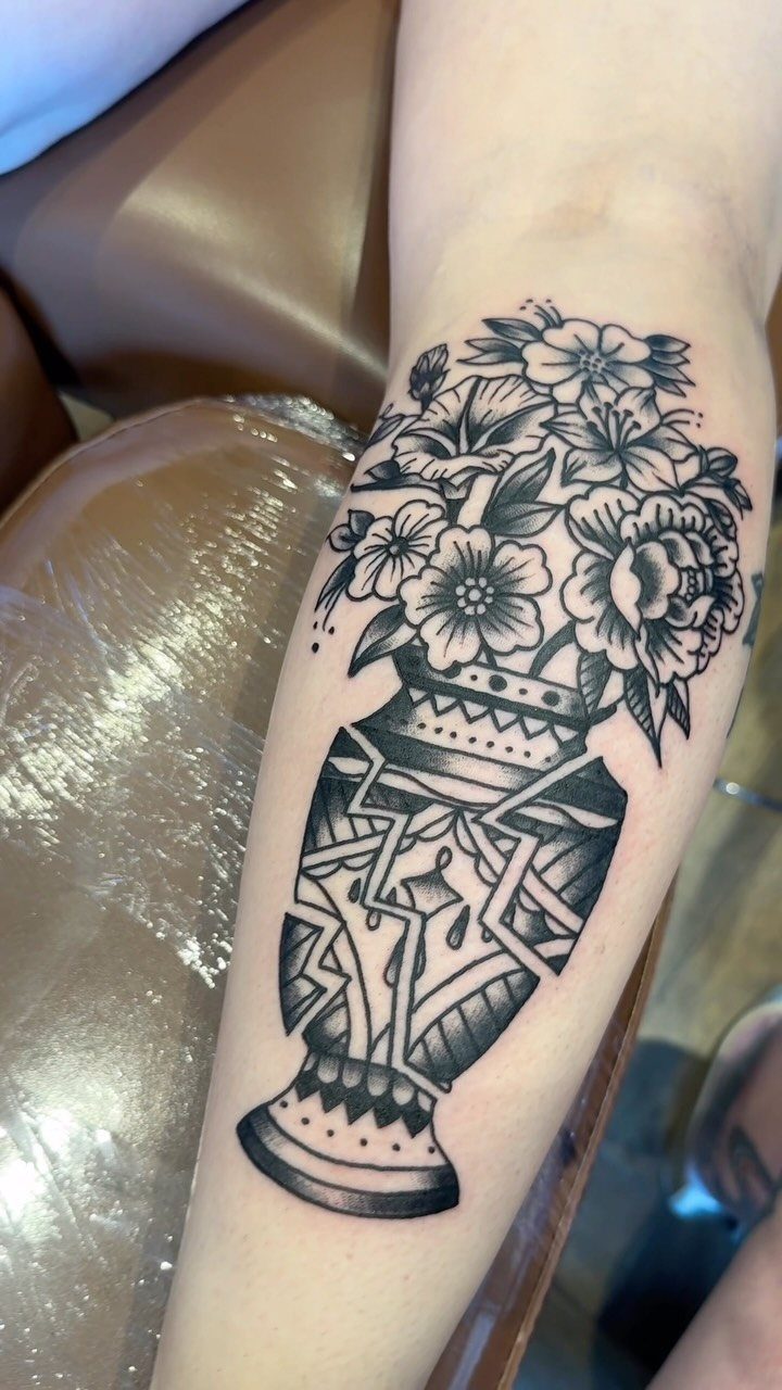 Black ink tattoo of a decorative vase filled with flowers on a forearm