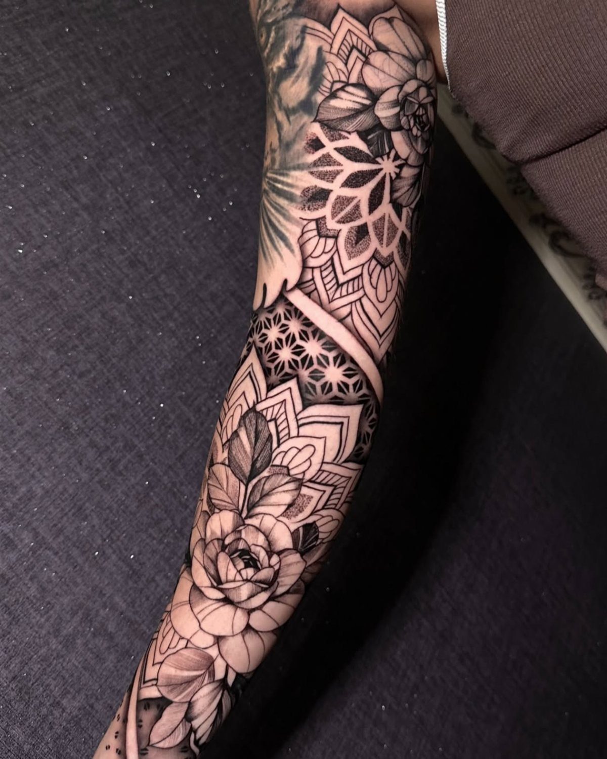Floral and geometric mandala tattoo covering a person's forearm in black ink.