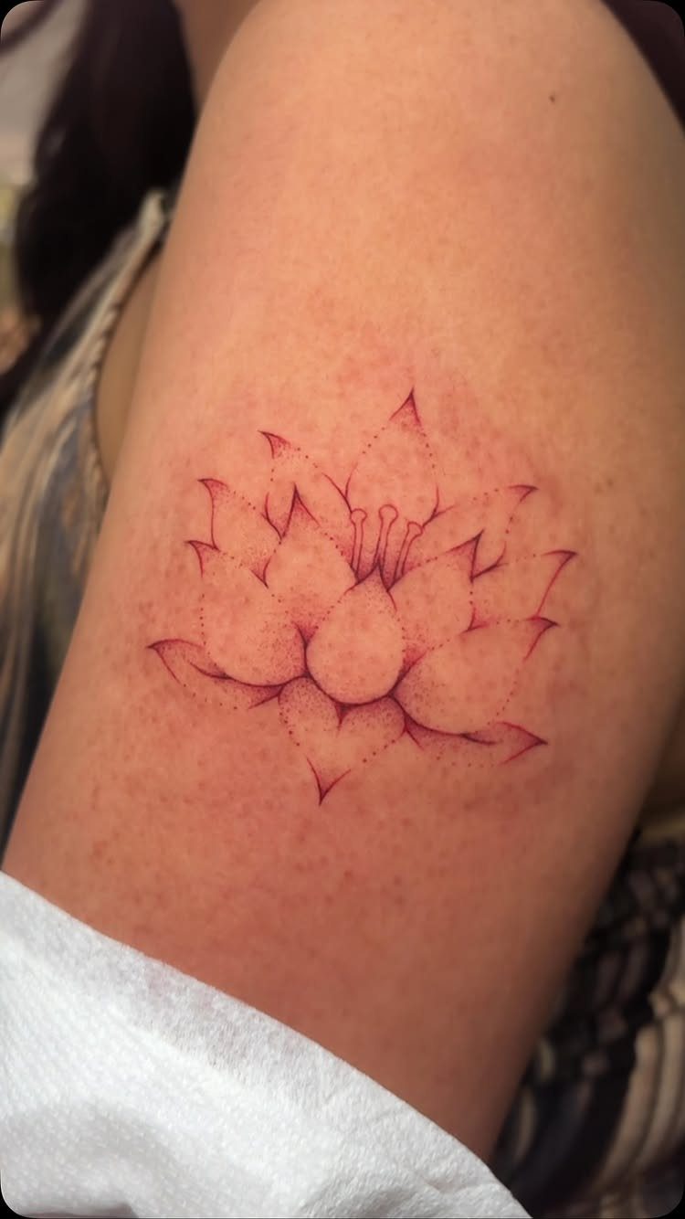 Red ink lotus flower tattoo on a person's upper arm with flushed skin.