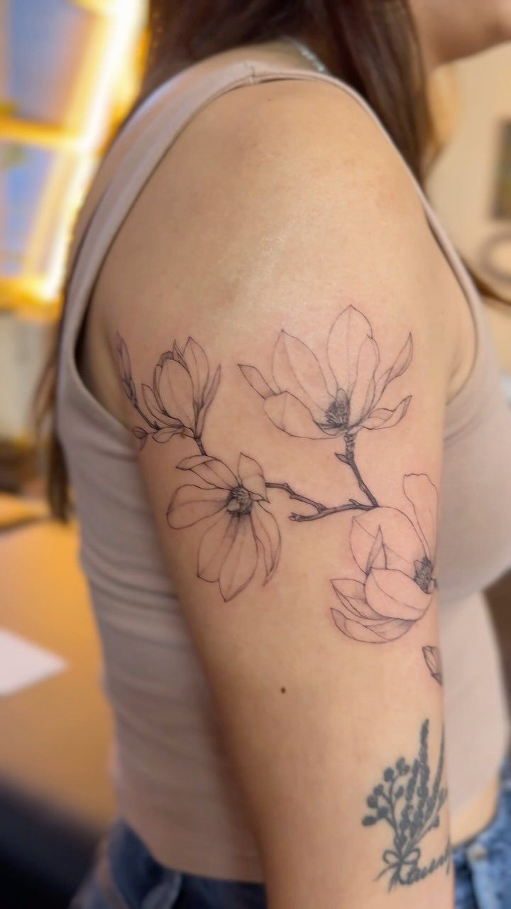 Magnolia flower tattoo with delicate lines on a person's upper arm