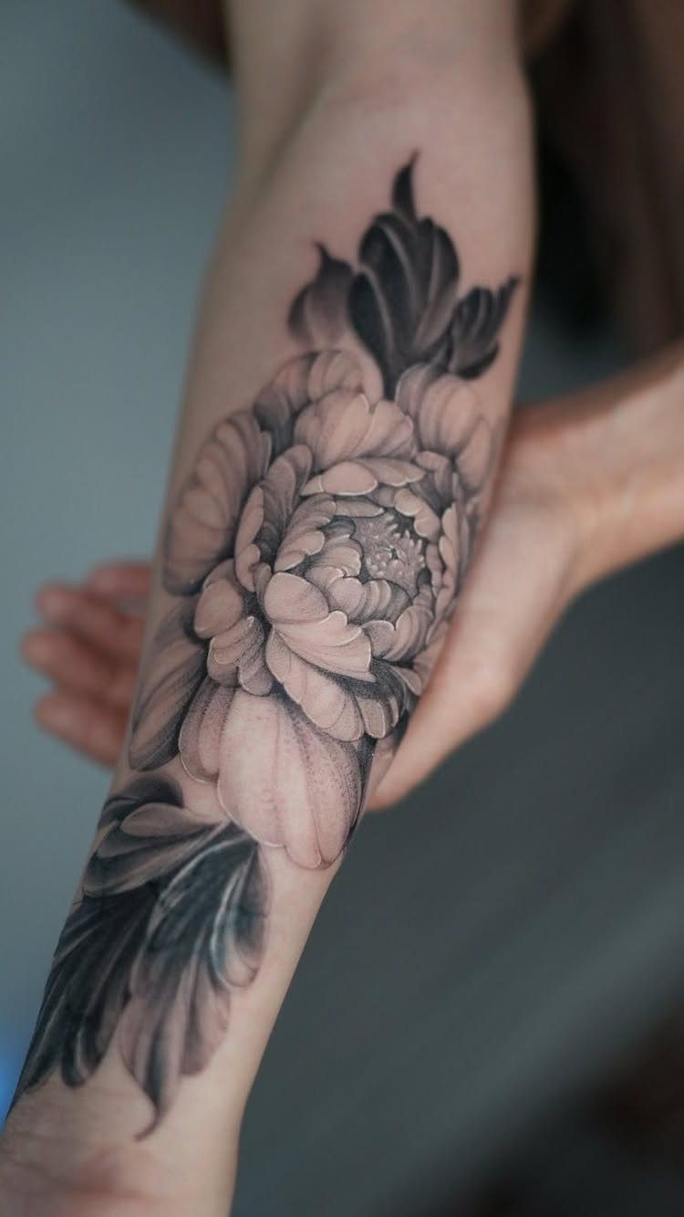 Peony flower tattoo in black and grey realism on a person's forearm.