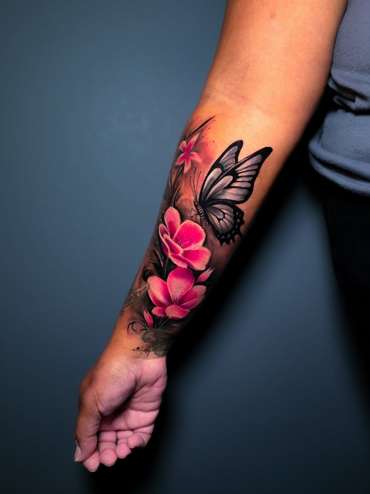 Detailed forearm tattoo of pink flowers and a black butterfly with realistic shading.