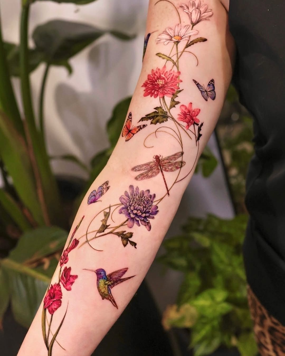 Colorful floral tattoo on a forearm with winding stems, leaves, and small birds.