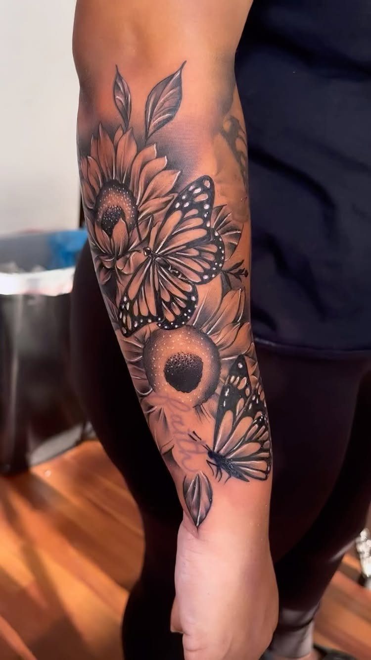 Sunflower and butterfly tattoo in black and grey ink on a person's forearm