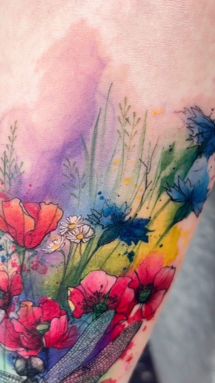 Watercolor flower tattoo with red poppies and blue blossoms on human skin