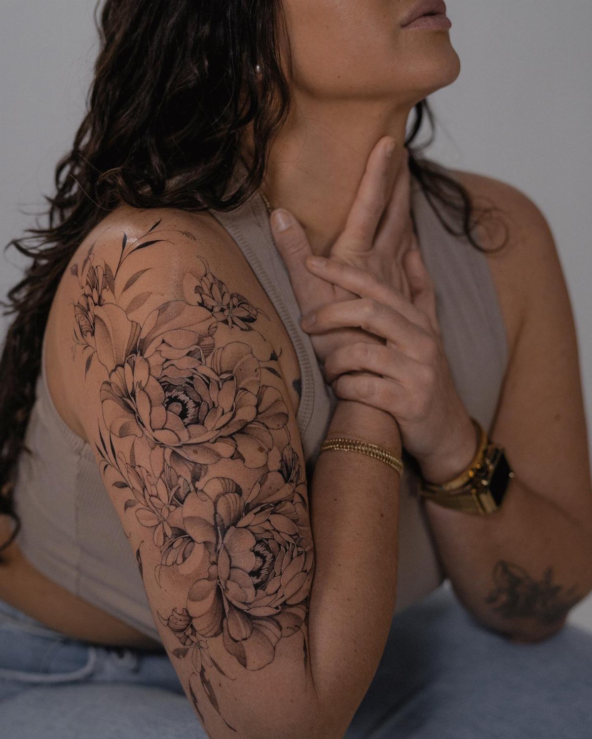 Large black and grey peony floral tattoo wrapping from shoulder down the upper arm.
