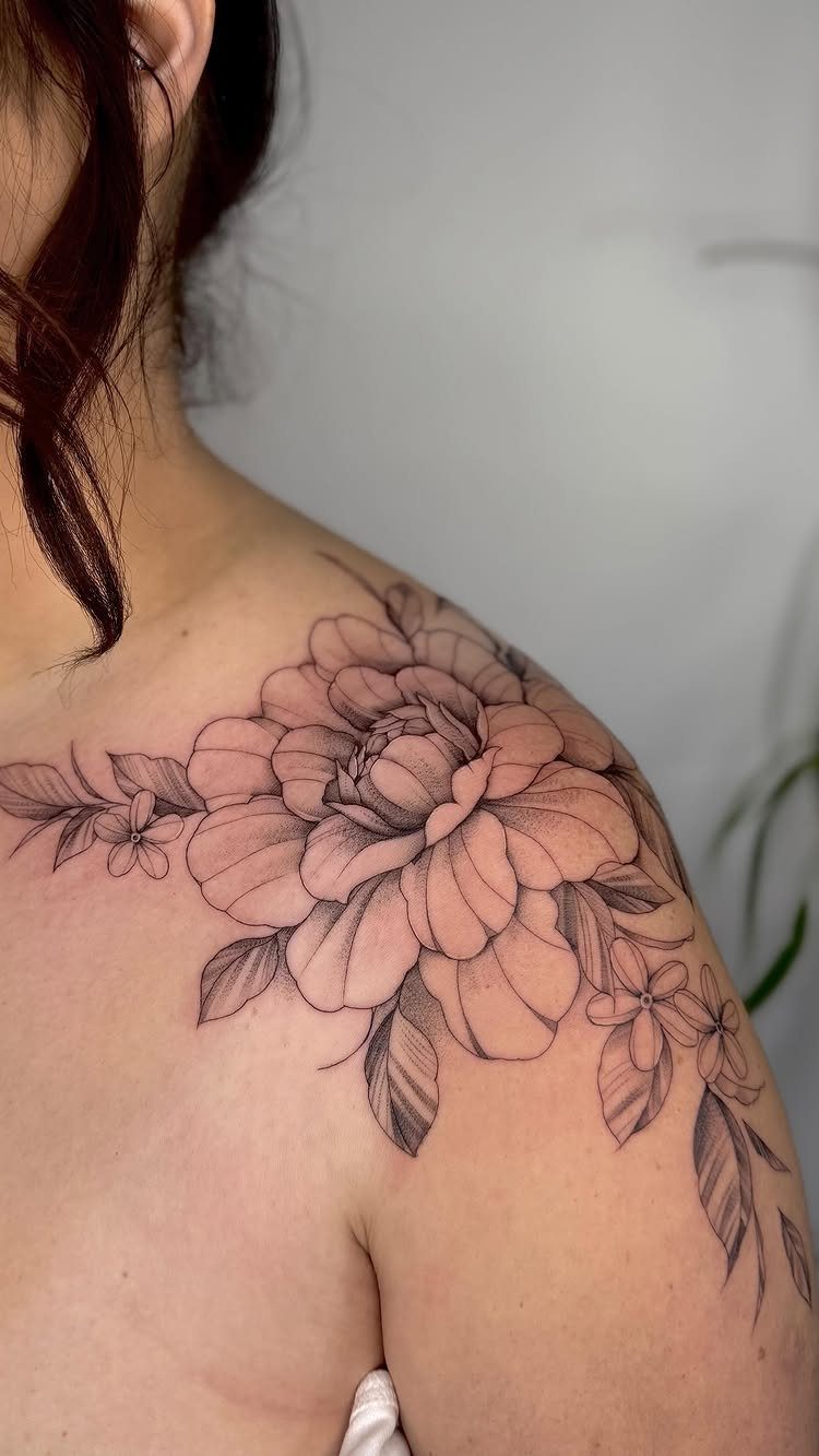 Large peony flower tattoo with leaves on a person's shoulder and upper arm.