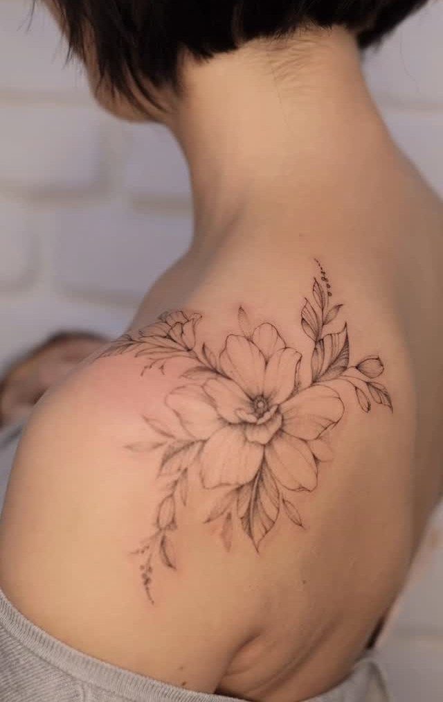 Floral tattoo on a shoulder featuring a large bloom and delicate botanical leaves.