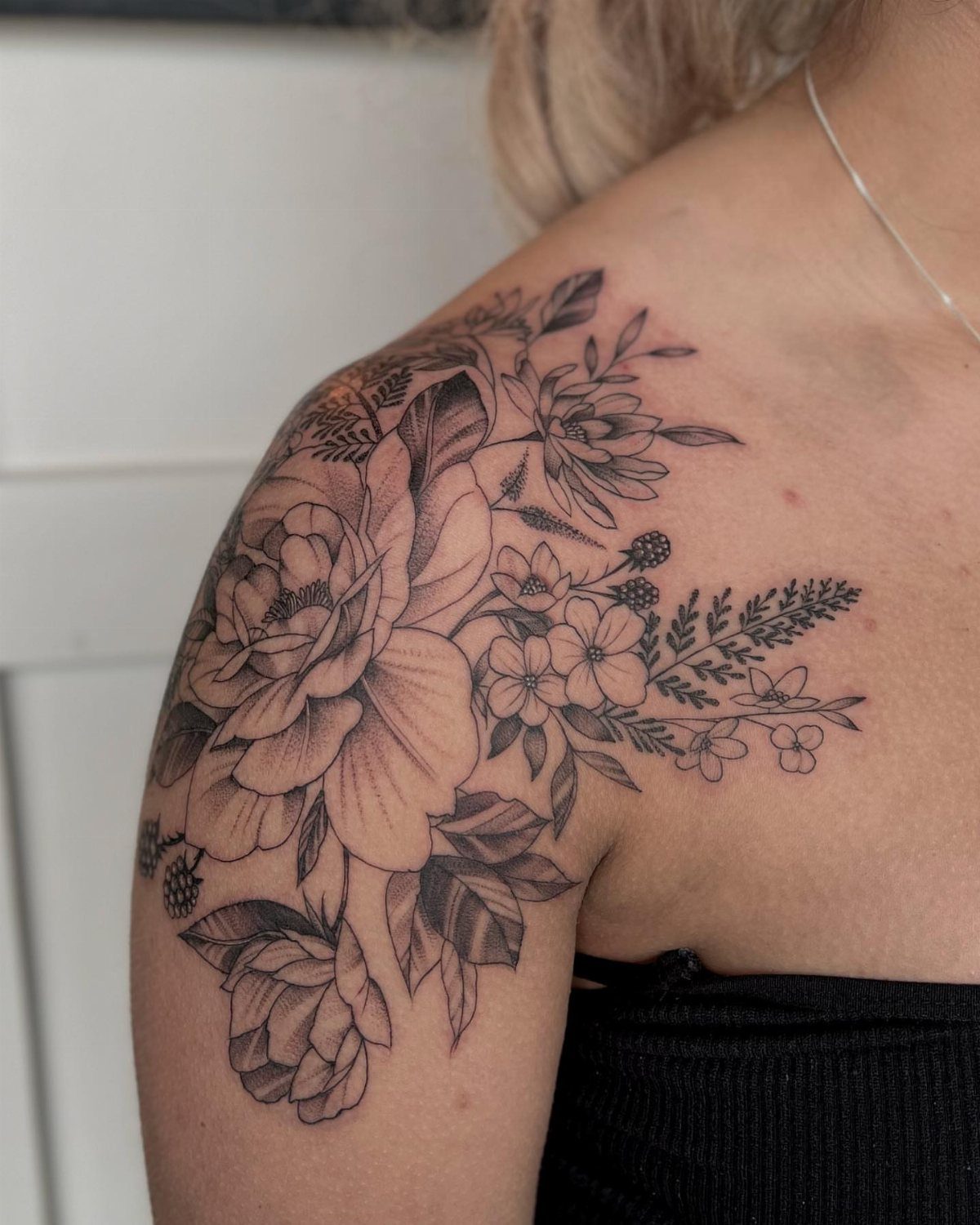 Floral tattoo on a shoulder featuring a large peony and wildflower clusters.