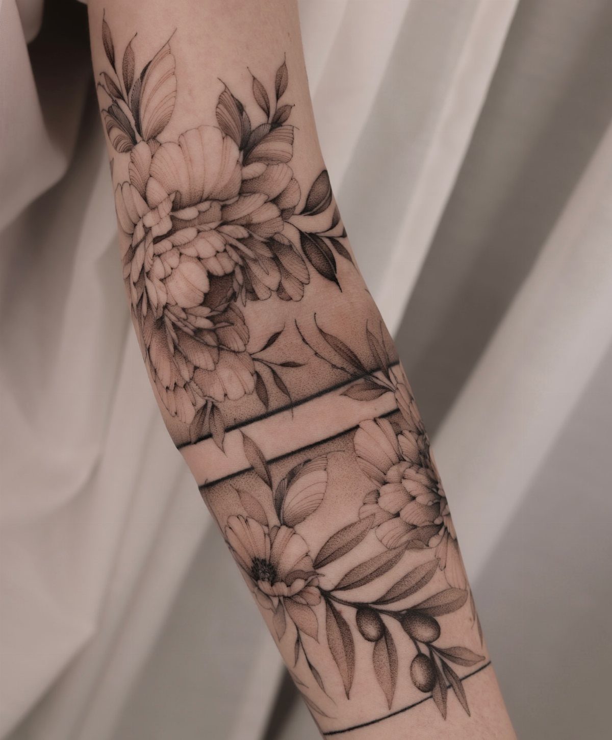 Black ink floral tattoo sleeve with peonies and thin geometric lines on an arm.