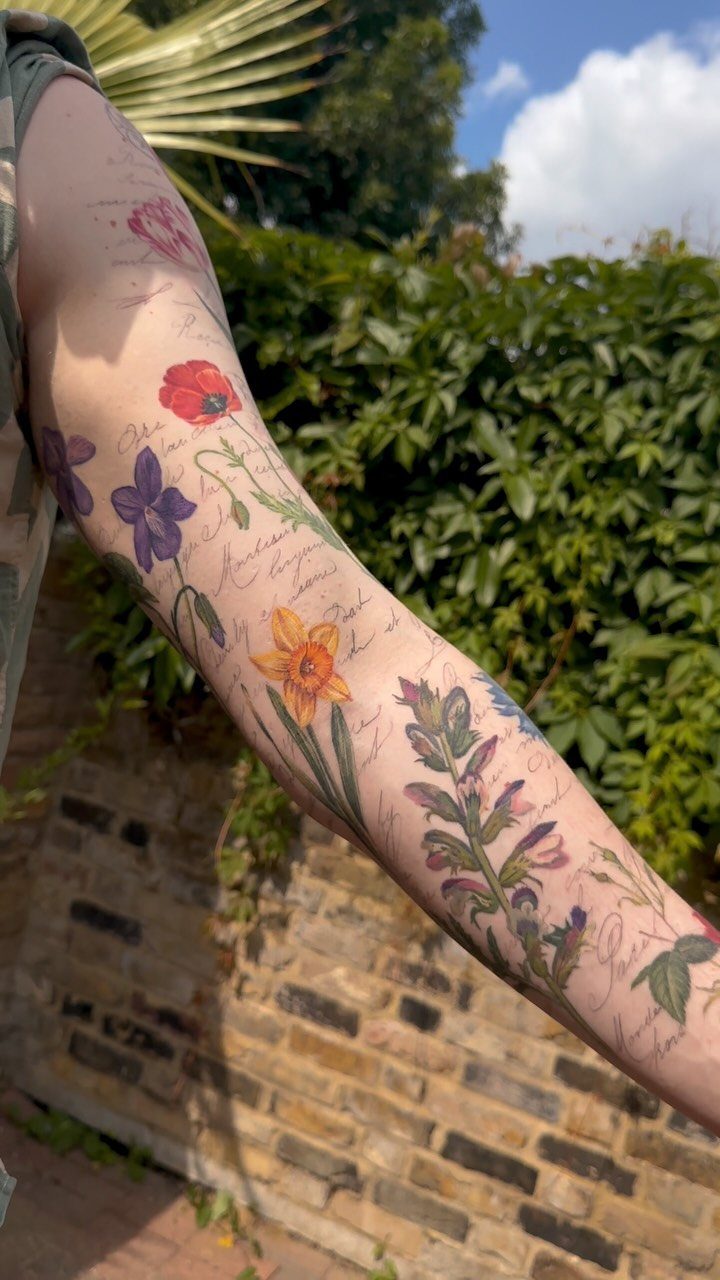 Colorful floral tattoo sleeve with various flowers and script on a person's arm.