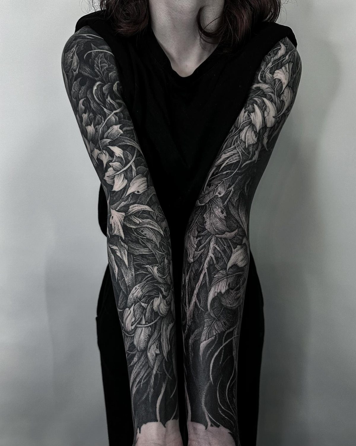 Full arm tattoo sleeves with dark floral patterns on a person in black.