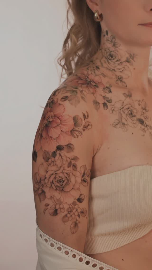 Floral tattoo sleeve with pink and black roses on a woman's shoulder and neck