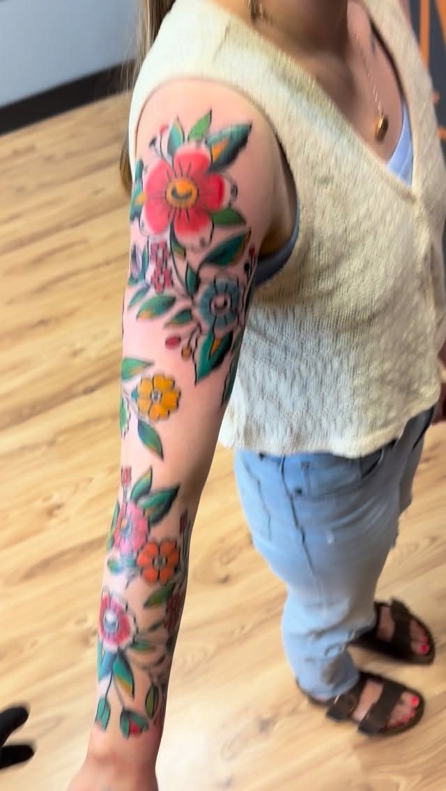 Colorful traditional floral tattoo sleeve with bold outlines on a person's arm.