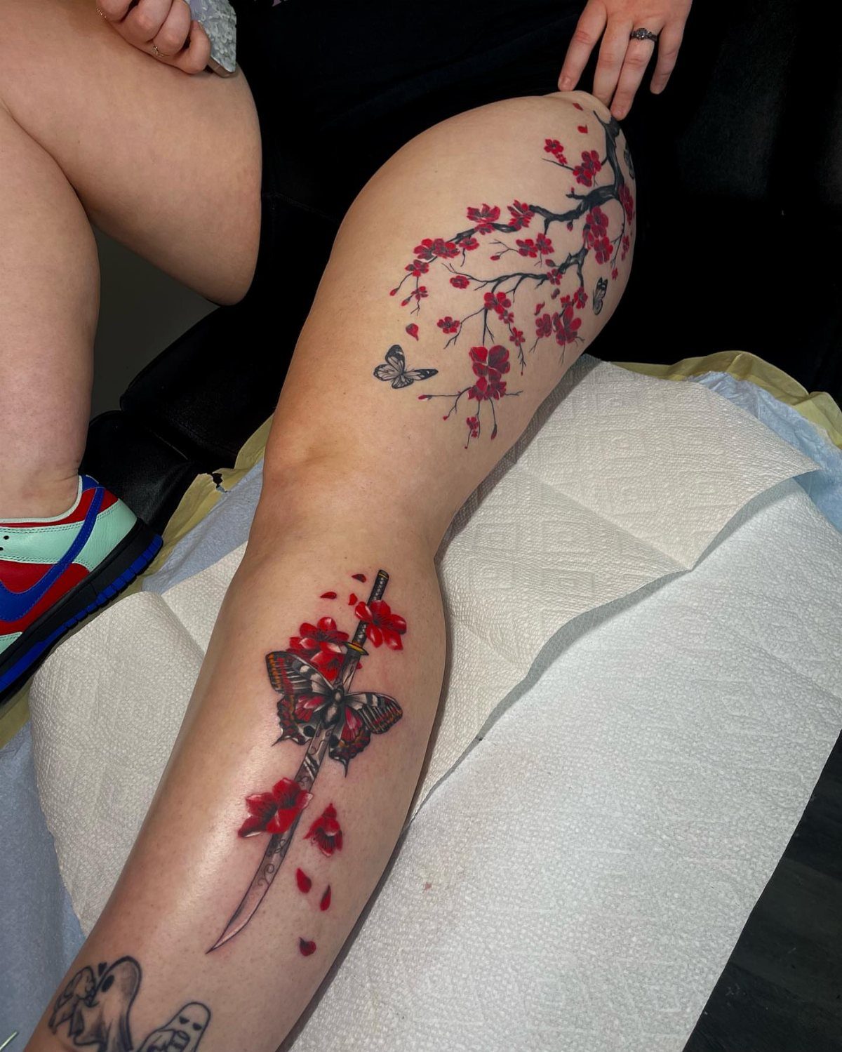 Cherry blossom branch tattoo with red flowers and butterfly on a person's thigh