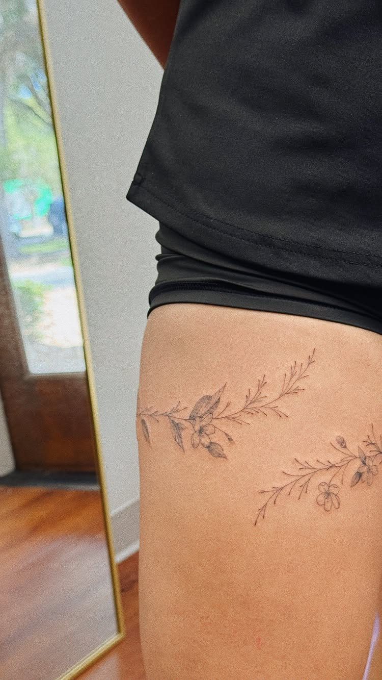 Delicate fine line floral tattoos with small blossoms on a person's thigh.