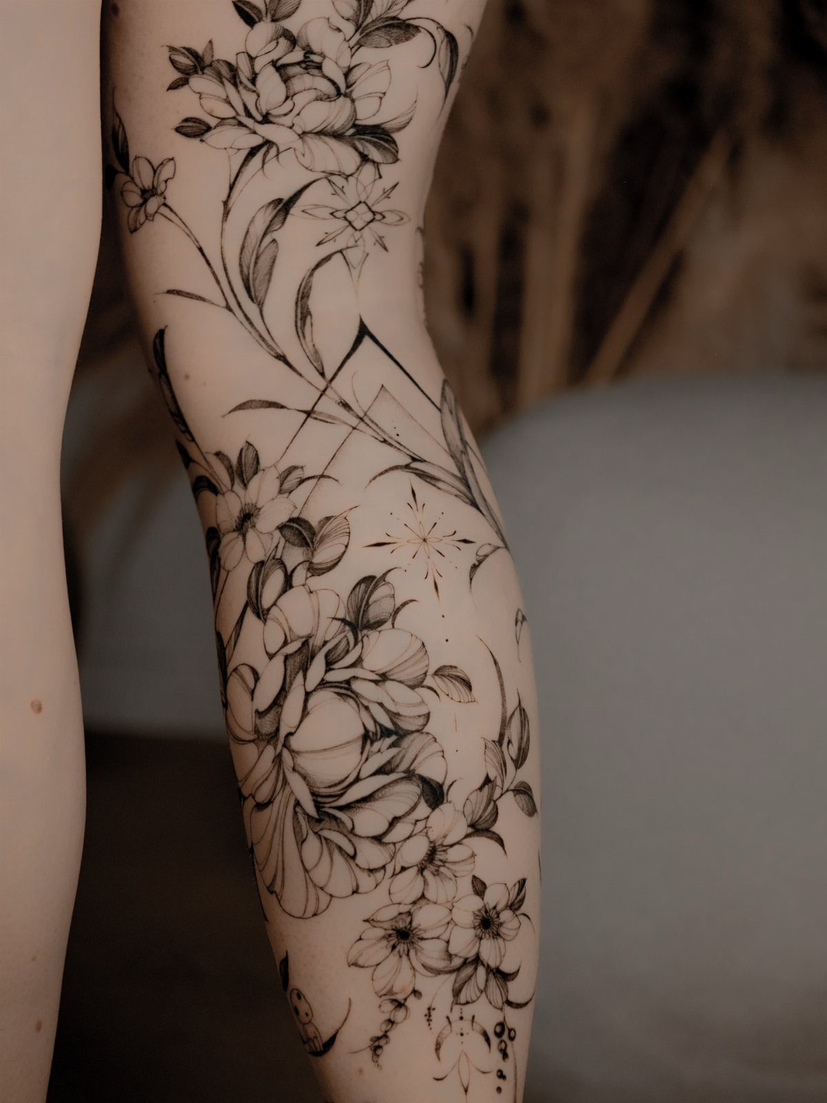 Floral thigh tattoo featuring peonies combined with geometric lines and star motifs.