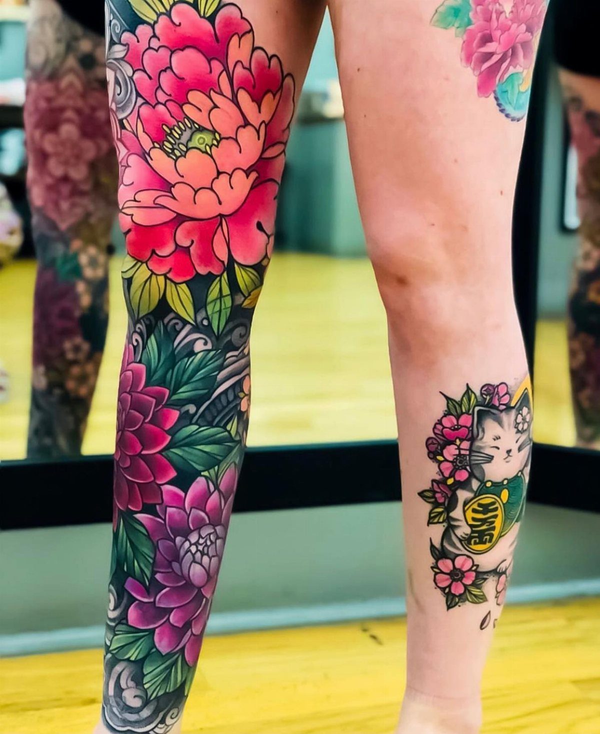 Vibrant full color floral tattoos of red and purple peonies on a thigh