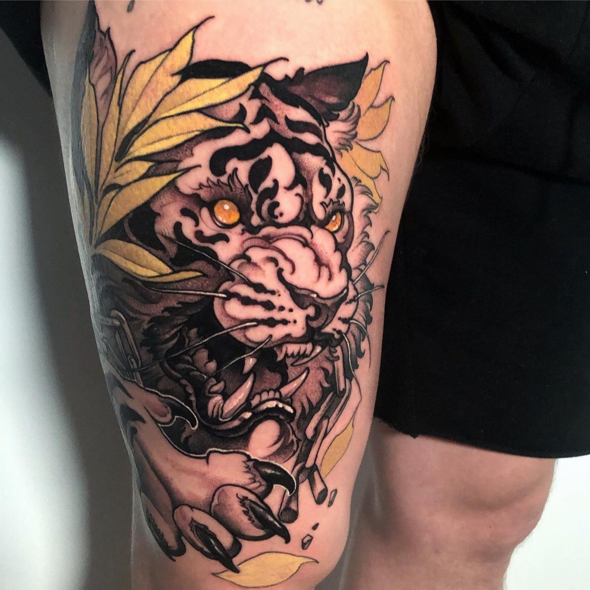 Neo-traditional tiger tattoo with yellow leaves on a person's thigh