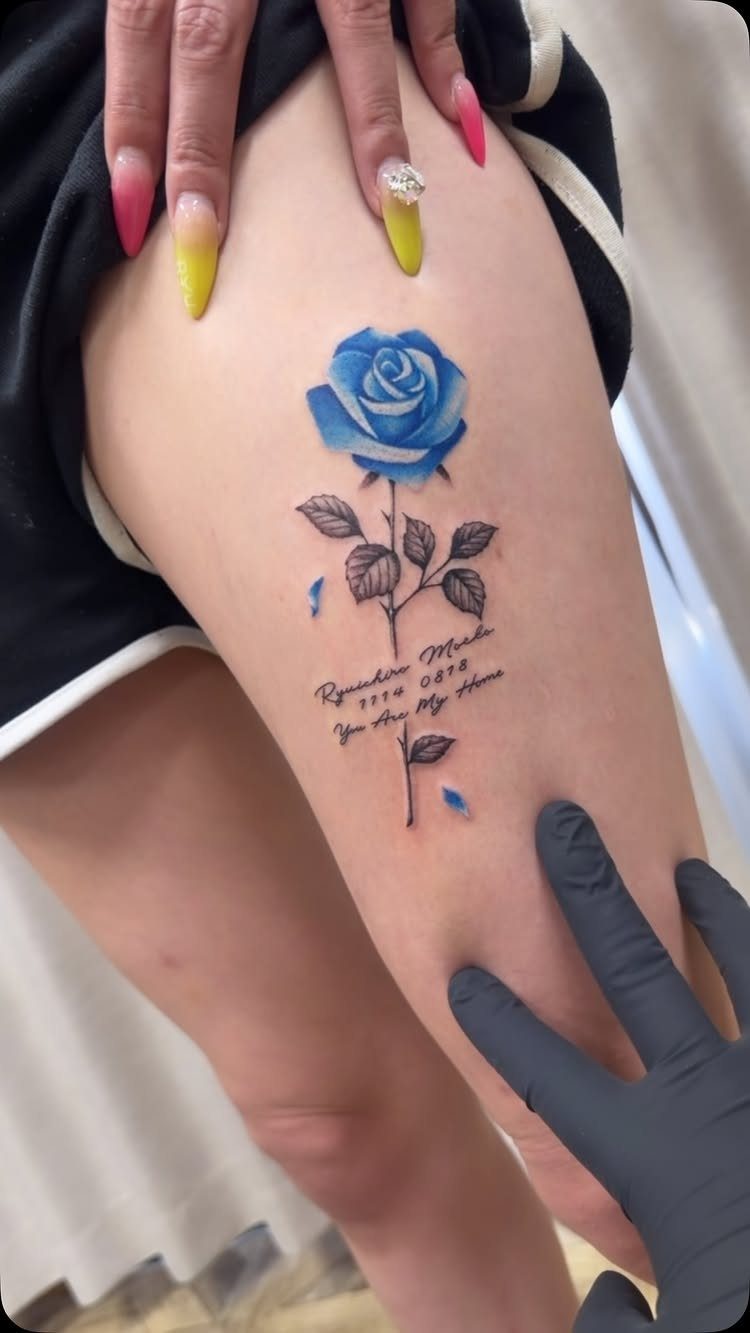 Blue rose tattoo with a stem and text on a person's thigh