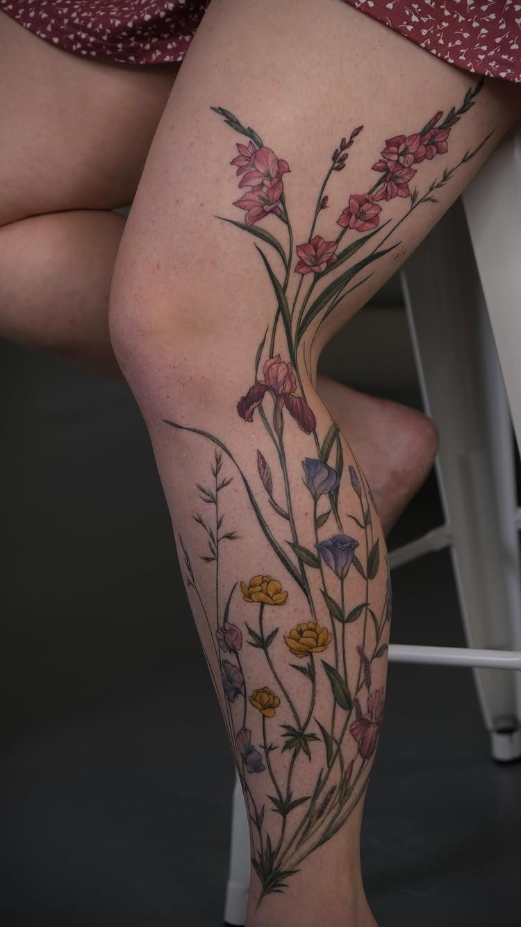 Colorful wildflower tattoo extending from the thigh down to the ankle on a leg.