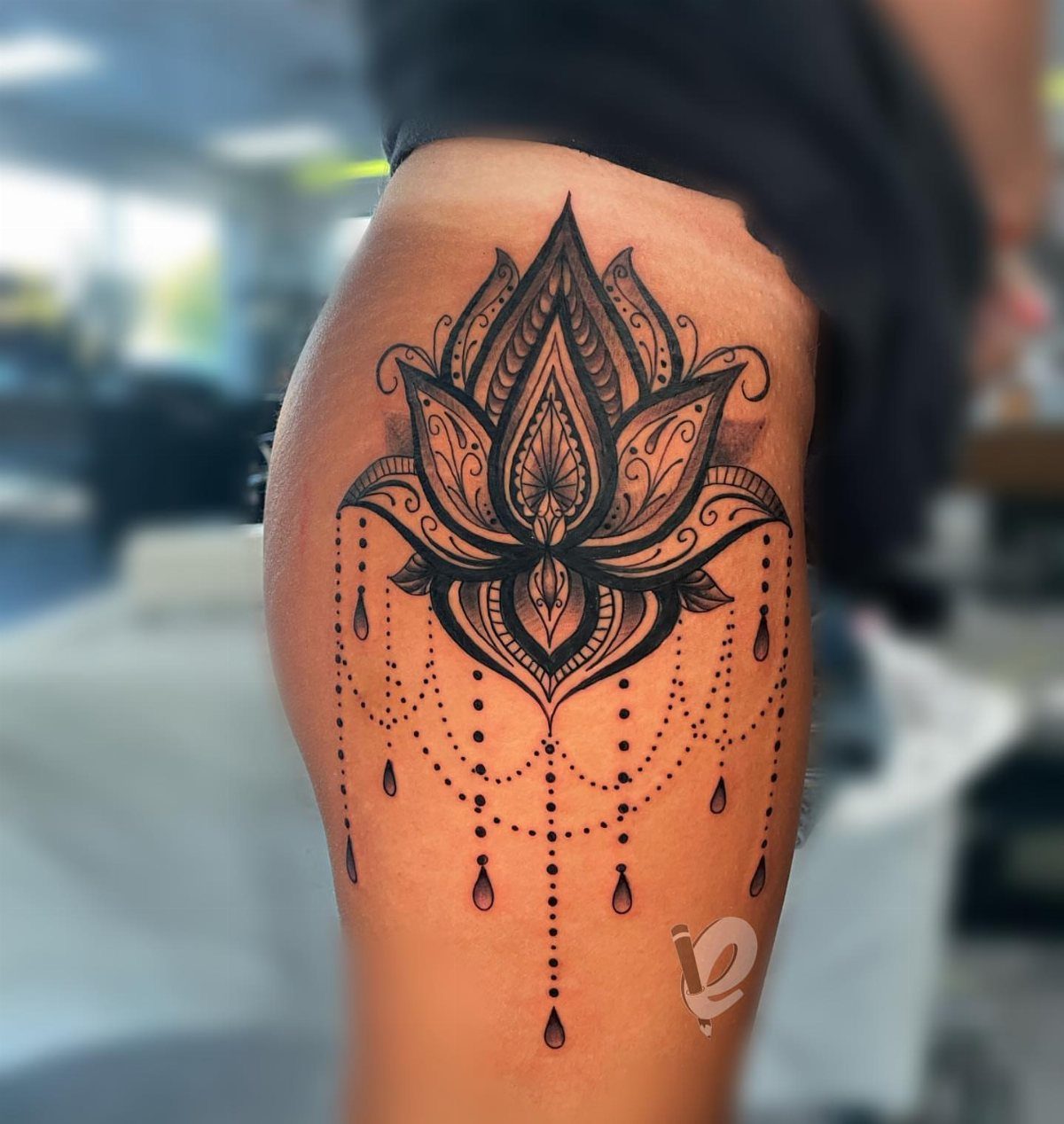 Symmetrical lotus flower tattoo with hanging beads on a person's thigh.
