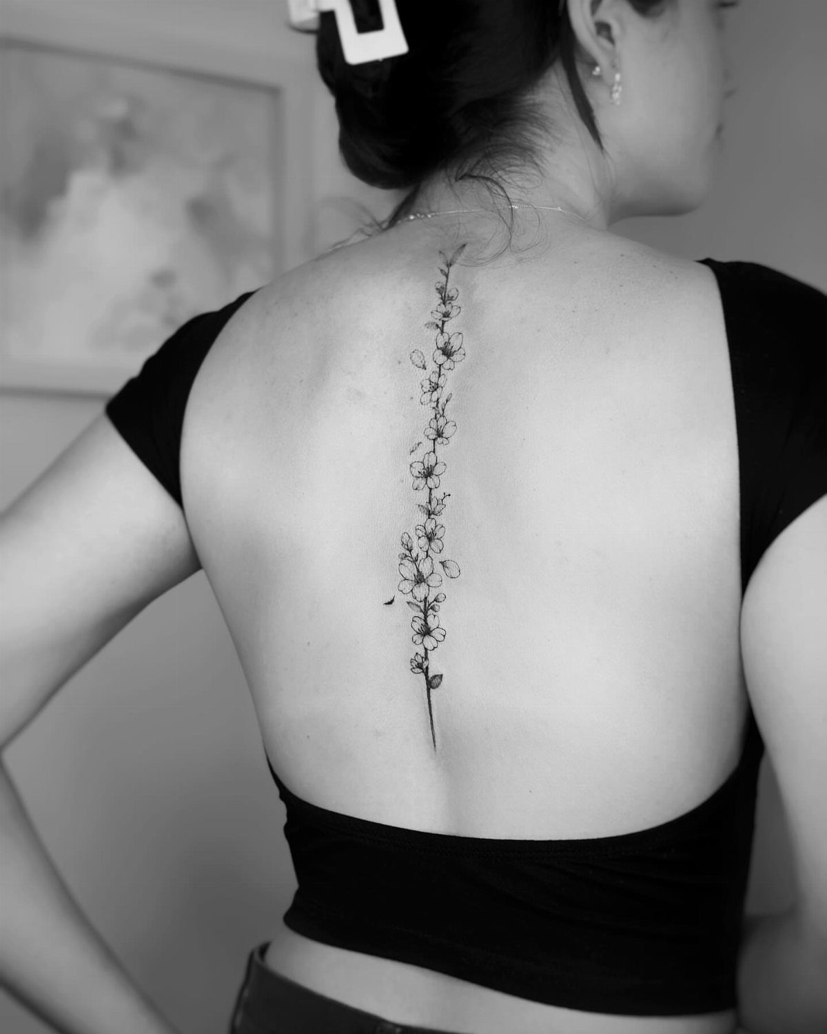 Vertical floral tattoo of small blossoms trailing down the center of a person's spine.
