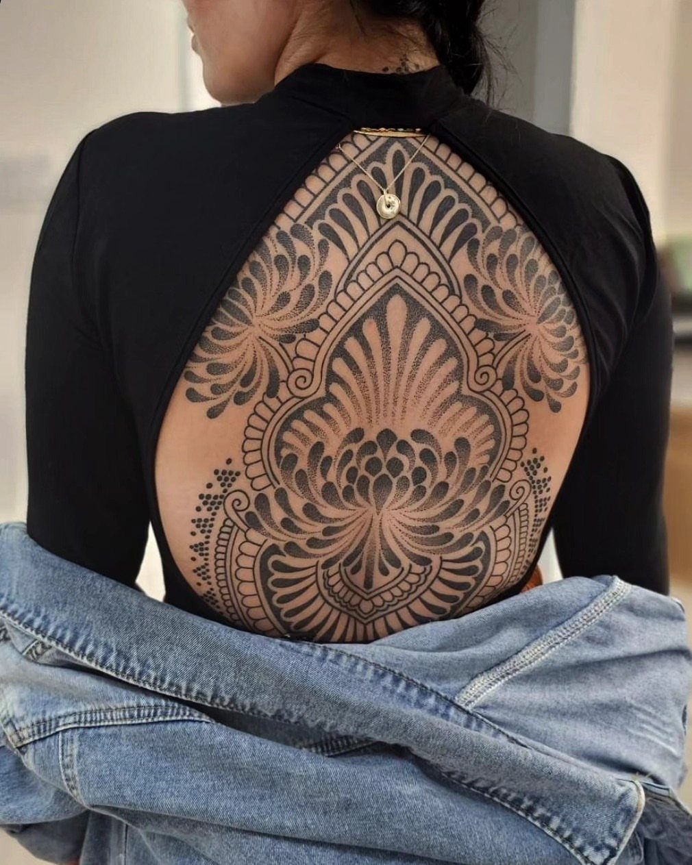 Symmetrical black ink floral dotwork tattoo covering the upper back of a person