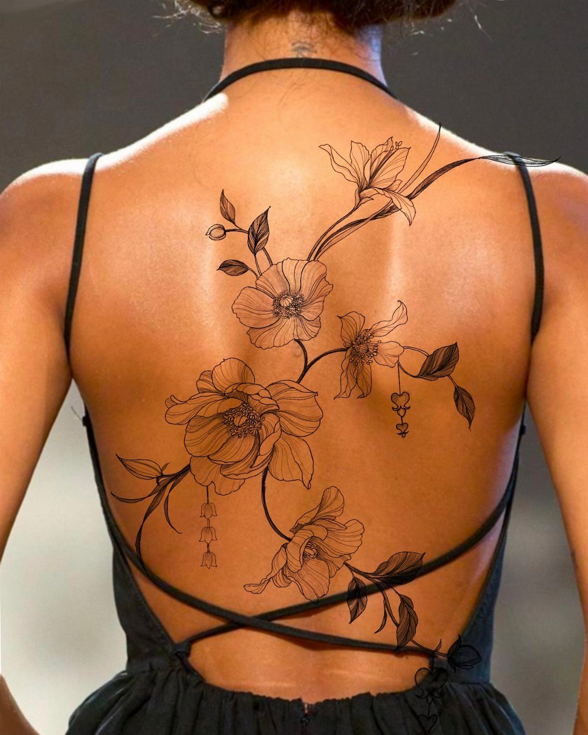 Large black ink floral tattoo cascading diagonally across a woman's bare back.