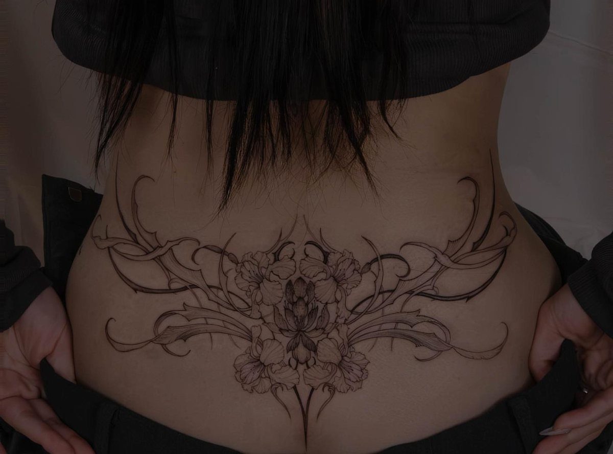 Symmetrical floral tattoo with swirling vines on a person's lower back